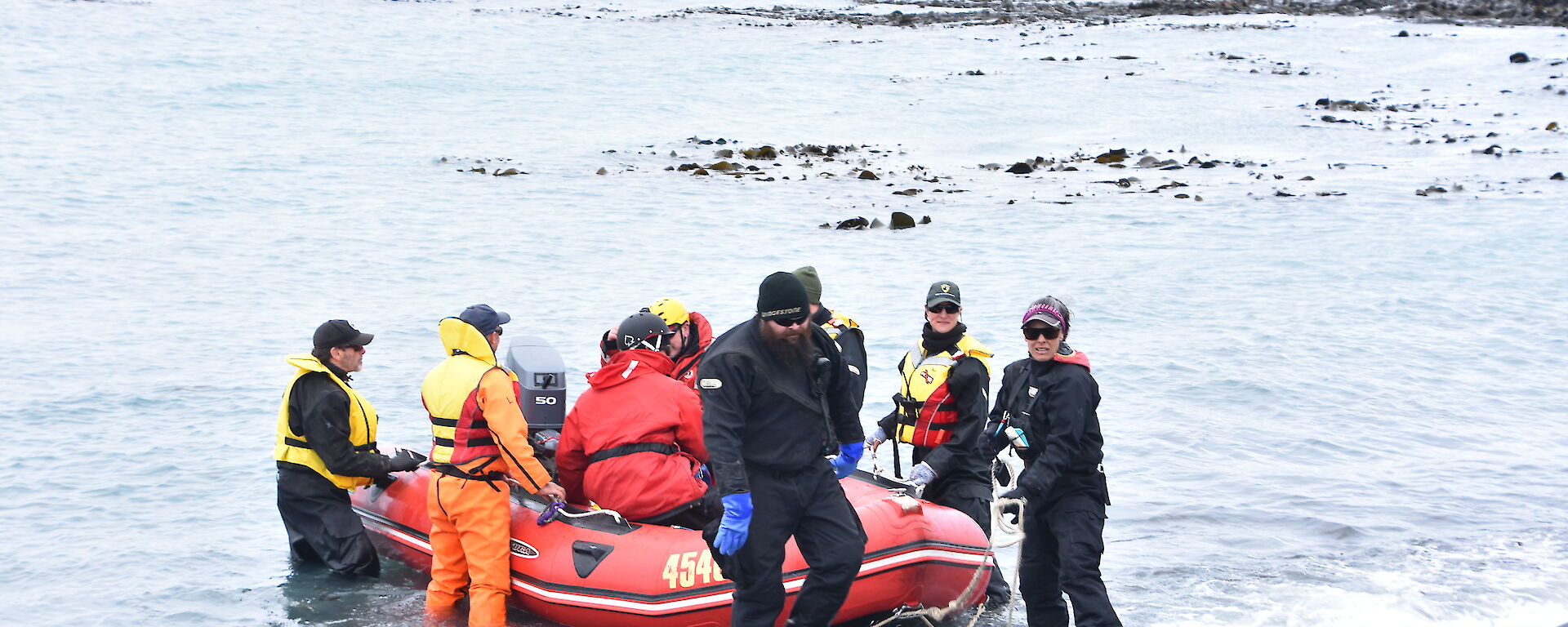A group of people on the waterfront help guide a small red boat to shore