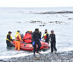 A group of people on the waterfront help guide a small red boat to shore