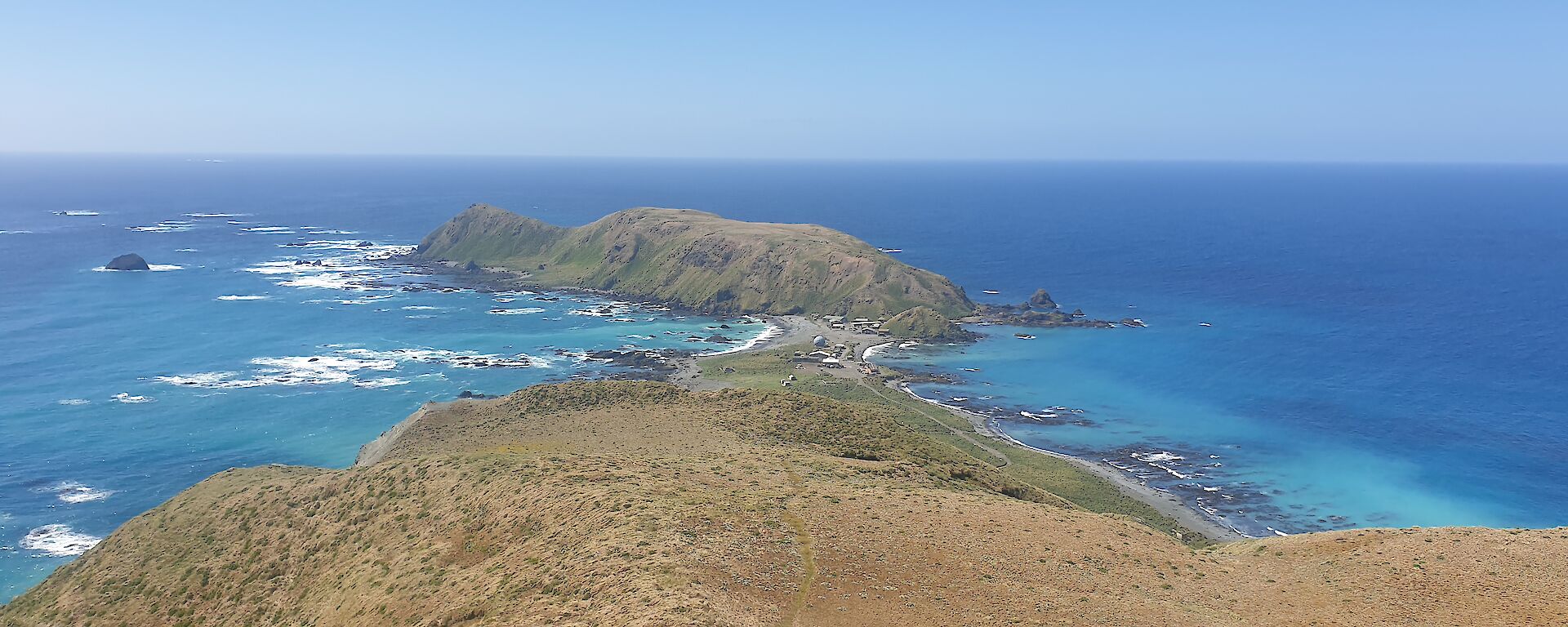 View from the top of a grassy hill, back towards the station amidst the blue sea