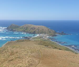 View from the top of a grassy hill, back towards the station amidst the blue sea