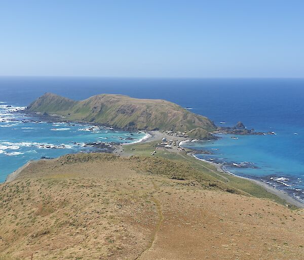 View from the top of a grassy hill, back towards the station amidst the blue sea