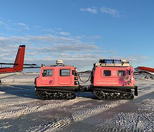 A man walking next to 2 planes and a pink Hagglunds on the sea ice