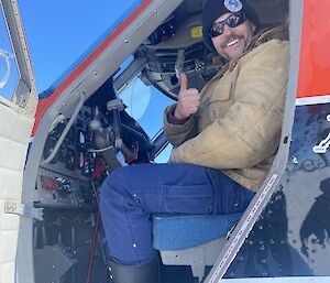 Looking in an open door at the front of a plane.  A man gives a thumbs up to camera.