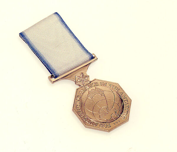 A Hexagonal medal with a blue and white ribbon. Wording on the medal reads "For outstanding service in the Antarctic"