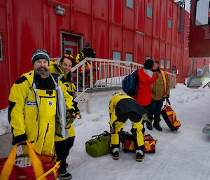 Some of the outgoing Casey team members standing outside with packed bags, preparing to board a bus for departure