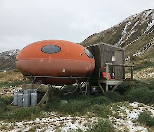 A round red hut on a platform above the snow covered green grass