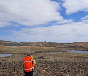 An expeditioner in hi vis walks across the open plains under cloudy skies