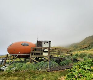 A red field hut sits amongst the green grass and grey clouds