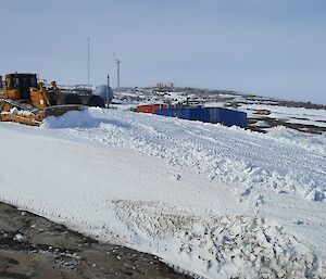 A dozer moving snow near colourful sheds at Mawson