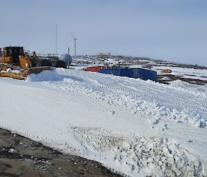 A dozer moving snow near colourful sheds at Mawson