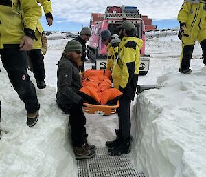 A group of expeditioners carrying a stretcher from the field into the medial facility through the snow