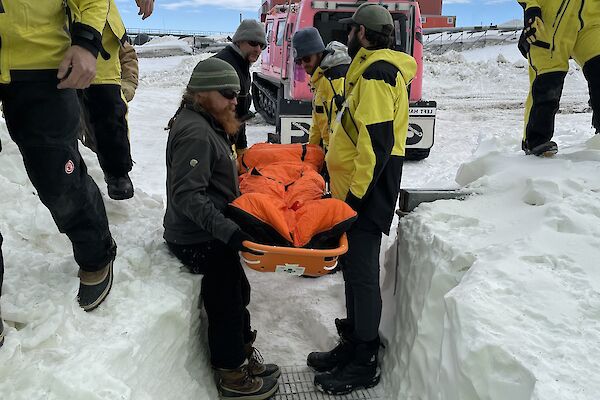 A group of expeditioners carrying a stretcher from the field into the medial facility through the snow