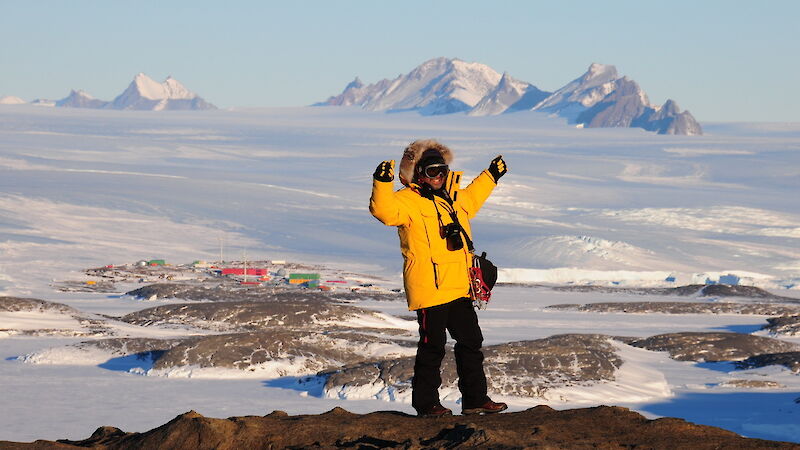 Person wearing yellow cold-weather gear raises their arms with station in the distant background