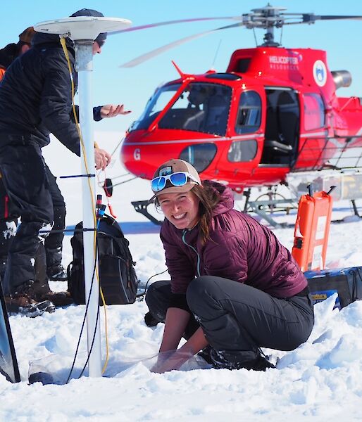 Expeditioners working in the snowy field, standing in front of a red helicopter