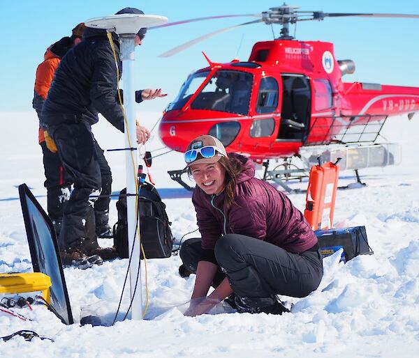 Expeditioners working in the snowy field, standing in front of a red helicopter