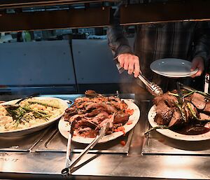 A diner serving himself from serving dishes laden with well-prepared food.