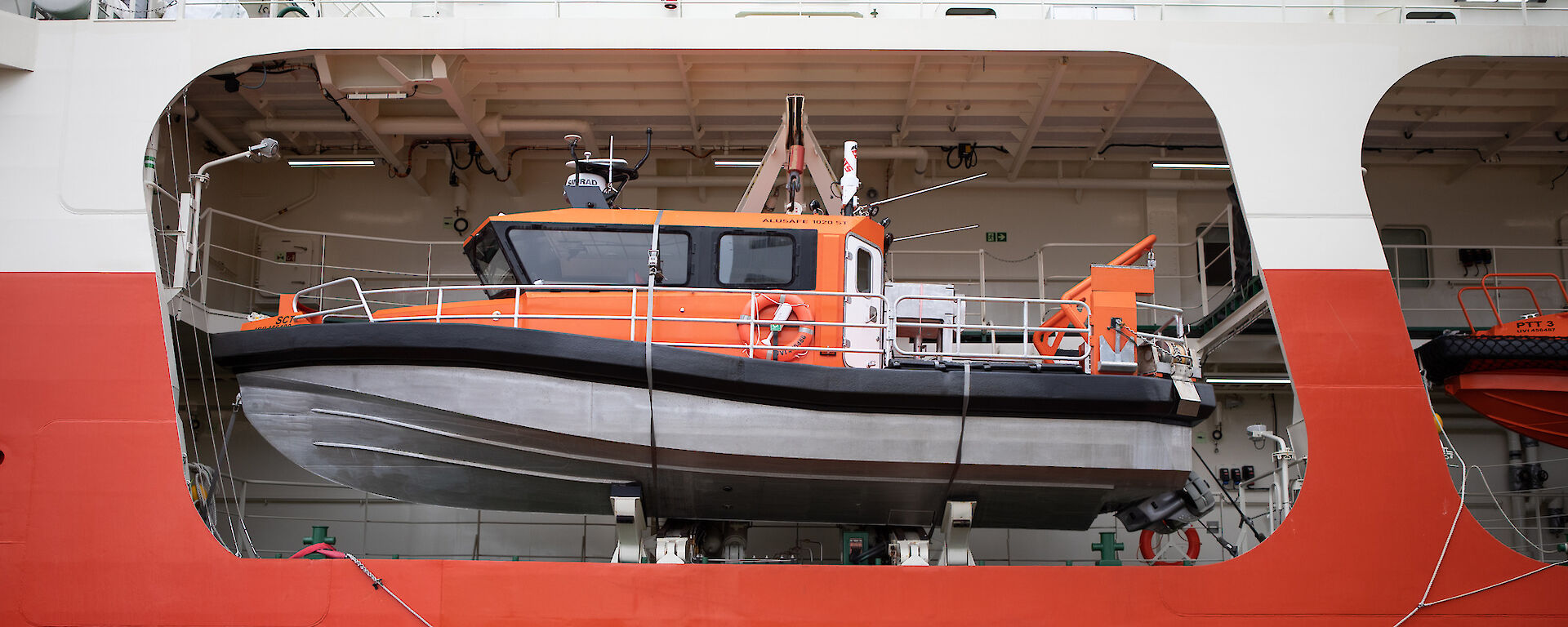 A small orange boat on board a large orange icebreaker ship.