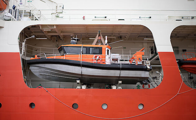 A small orange boat on board a large orange icebreaker ship.