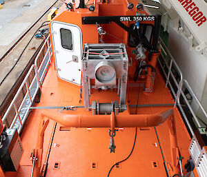 A small orange boat on board a large orange icebreaker ship.
