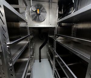 Inside of a walk-in freezer room with empty stainless steel shelves.