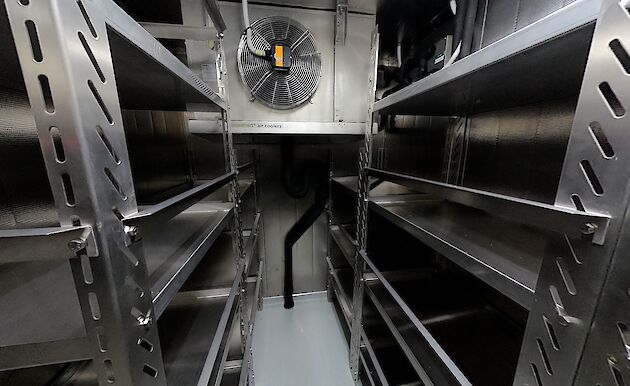 Inside of a walk-in freezer room with empty stainless steel shelves.