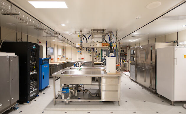 A brightly lit room contains sinks, desks, cabinets and scientific equipment.