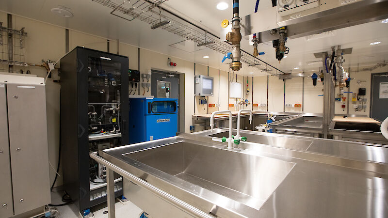 A brightly lit room contains sinks, desks, cabinets and scientific equipment.