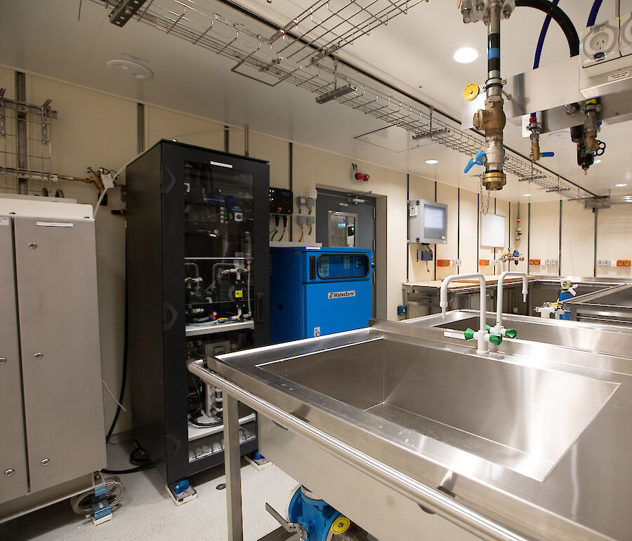 A brightly lit room contains sinks, desks, cabinets and scientific equipment.