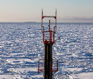 View over sea ice looking past a red ship's foremast .
