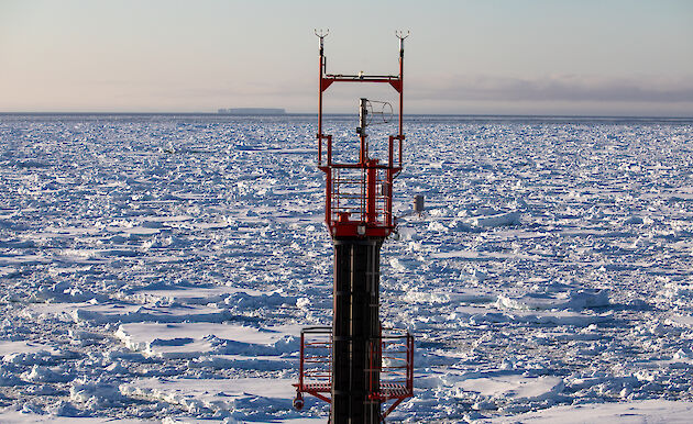 View over sea ice looking past a red ship's foremast .