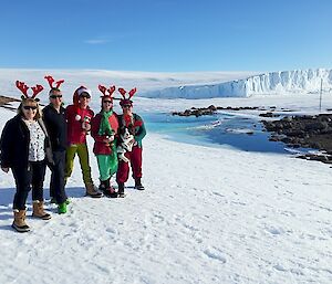 Five ladies dressed in Christmas outfits stand out on the snow under blue skies
