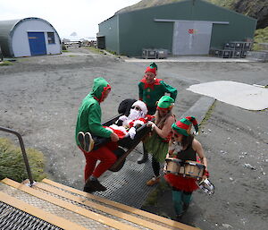 A person in a Santa suit is carried up the stairs whilst sitting in a wheelbarrow