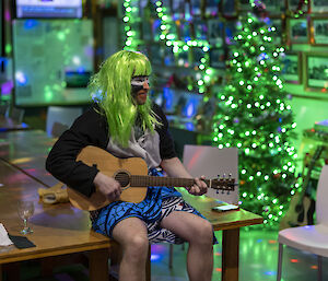 A person in fancy dress and a green wig plays the guitar