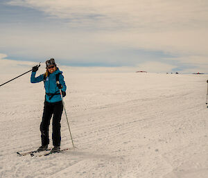 Two skiers on the track, one several metres ahead of the other. The skier in front wears a blue jacket and is smiling and waving at the person taking this photo.