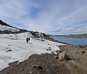 2 men walking on ice next to a large lake