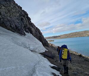 A group of hikers walking between some ice and a lake