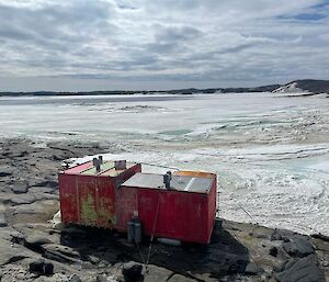 small red hut on rocks looking out on sea ice