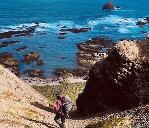 A person walks down a rocky path towards the sea