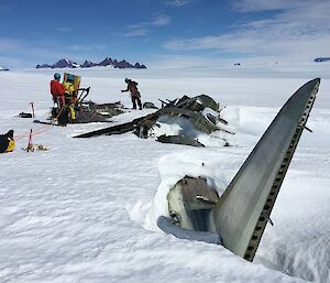 Expeditioners at the site of a wrecked Russian aircraft with the ranges of the Framnes Mountains in the background