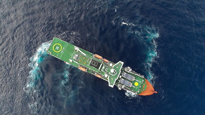 An aerial drone photo. Aerial view of an icebreaker ship in open water. Trails of bubbles and light blue water show how the ship is turning in the water.