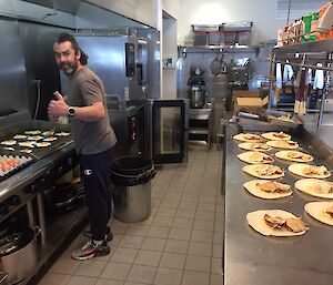 A man standing in a commercial kitchen making bacon and egg wraps