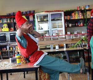 A man dressed as Santa's elf sitting on the edge of a table yelling instructions to a team