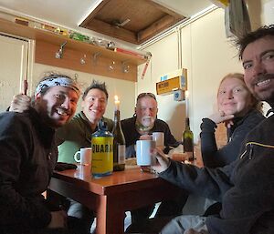 Five people sitting around a table having a hot drink smiling at the camera
