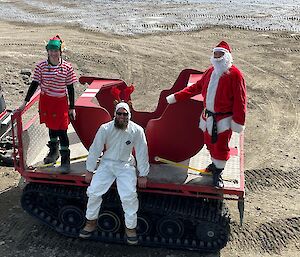 Three people dressed up as Santa, an elf and a reindeer on a tray with a Santa sled