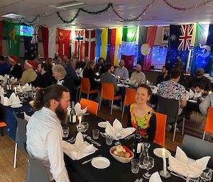 Two long tables set with black table clothes and world flags on the windows and people sitting around.