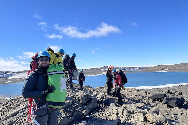A team of people standing in search and rescue harnesses on top of rocky mountain with water and ice in the background