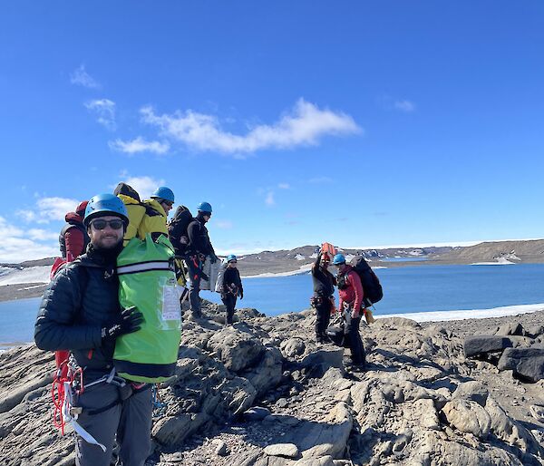 A team of people standing in search and rescue harnesses on top of rocky mountain with water and ice in the background