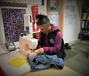 A lady works on some blue jeans on a sewing machine
