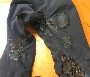 A dark coloured pair of pants with lots of repairs all over them