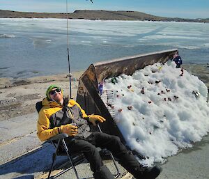 A man in a deck chair soaking up the warmth of the sun at Mawson on Australia Day with the flag flying behind him